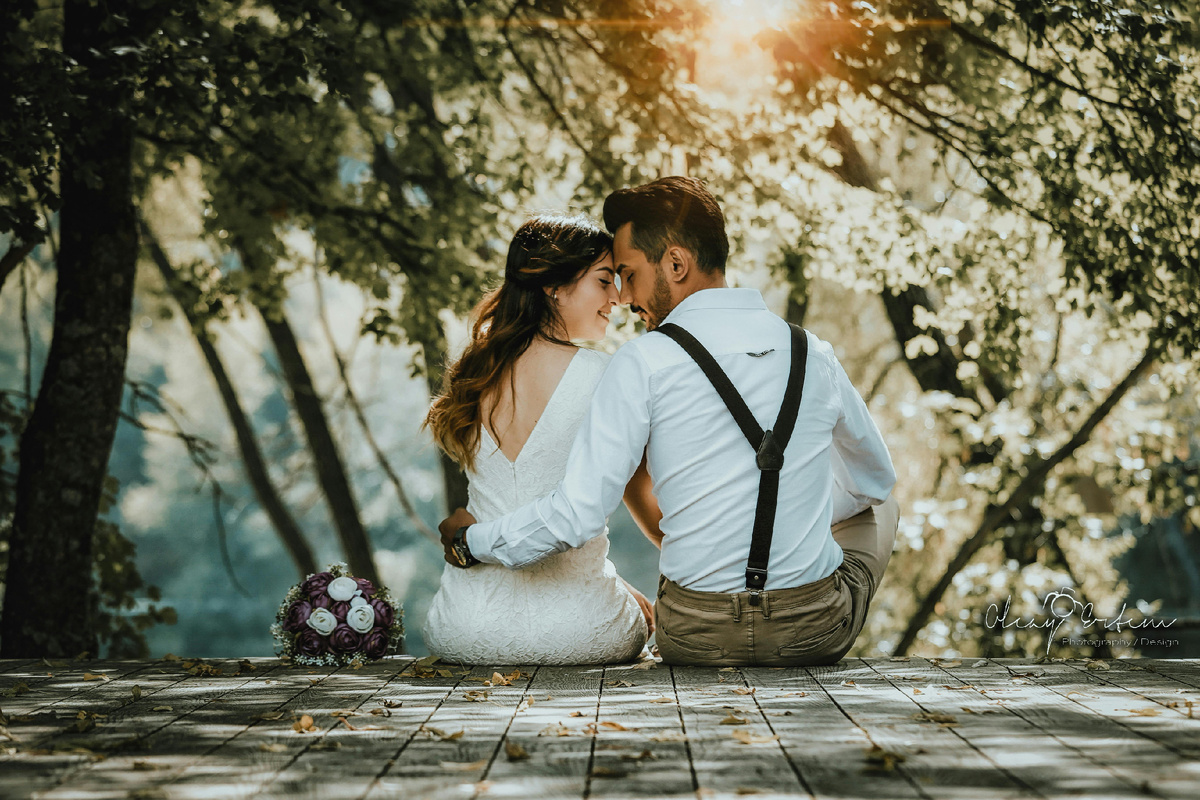 Пара сидит на деревянной площадке в парке и обнимается на фоне солнечного света и деревьев