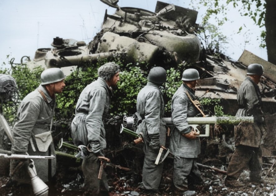 Немецкие десантники осматривают подбитый танк «Шерман» в Нормандии. Они несут 88-мм противотанковое орудие RPzB 54 Panzerschreck (справа) и противотанковые гранатомёты Panzerfaust 60.