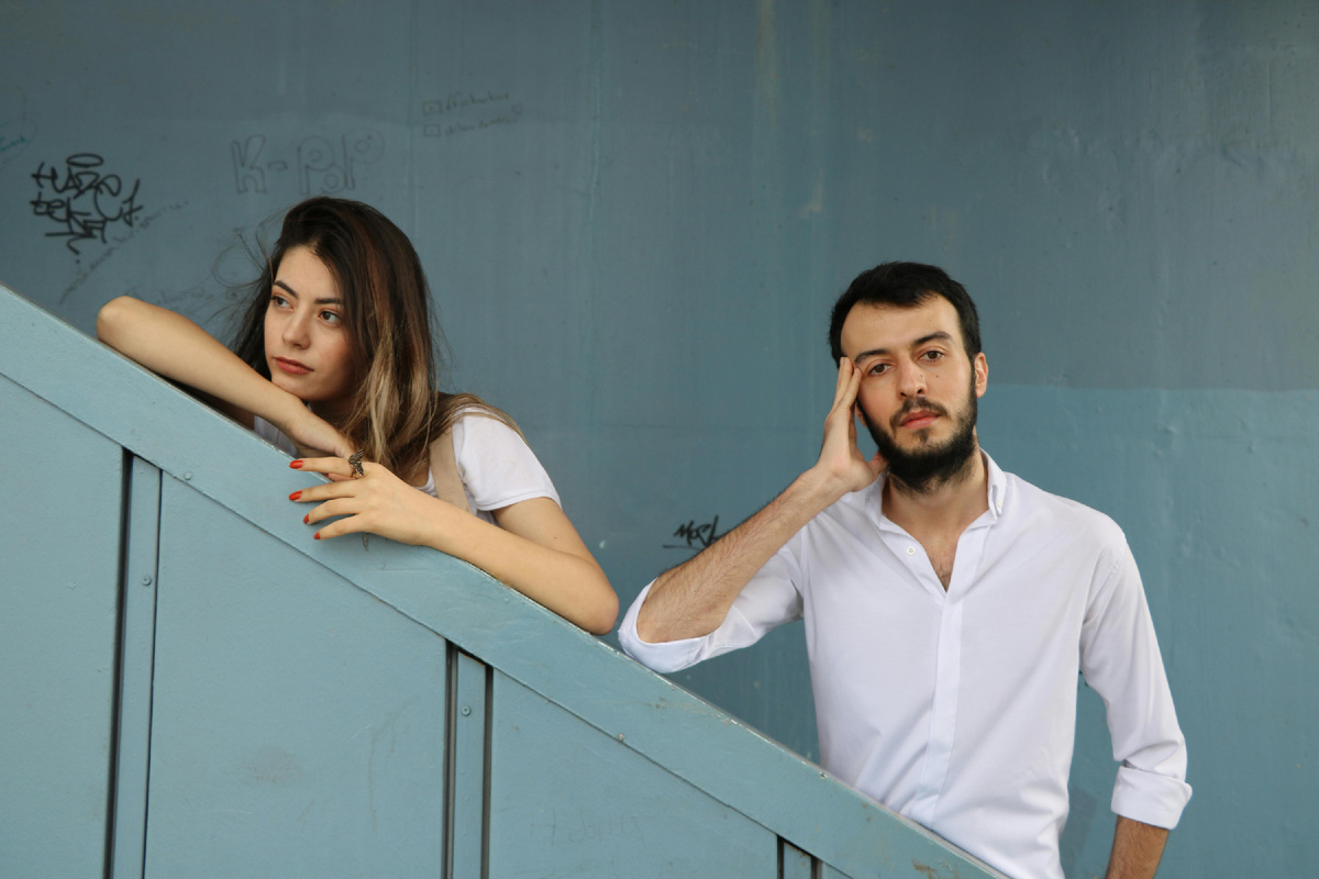 Молодая пара стоит на лестнице и задумчиво смотрит в разные стороны, передавая момент размышления и поиска взаимопонимания в отношениях.