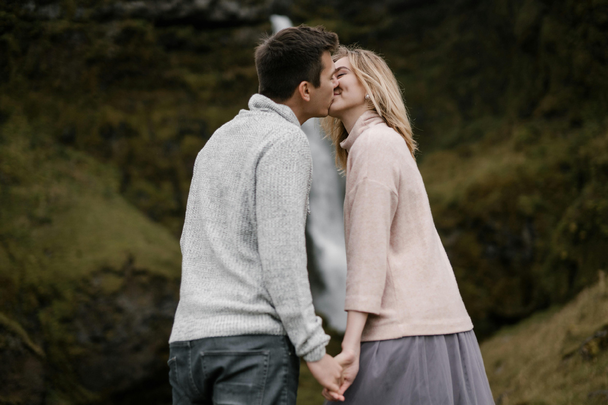 Пара держится за руки и целуется на фоне водопада