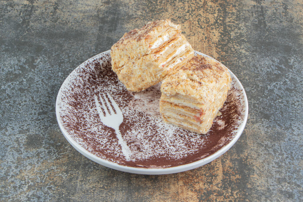    A white plate with two pieces of Napoleon cake and cocoa powder. High quality photo Журналист