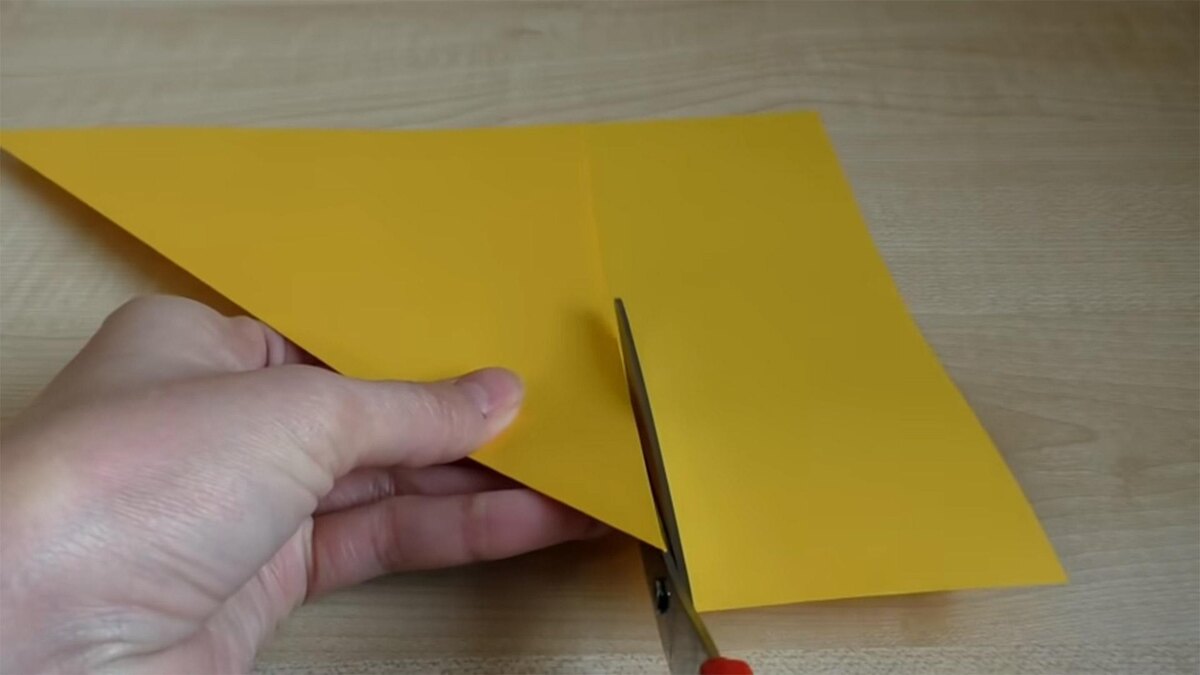    Из прямоугольного листа А4 нужно сделать квадратный. Для этого складываем короткую сторону листа с длинной по диагонали. Лишнюю часть отрезаем ножницами. Если у вас изначально квадратный лист бумаги, пропустите этот шагУмничка Ульяна / YouTube