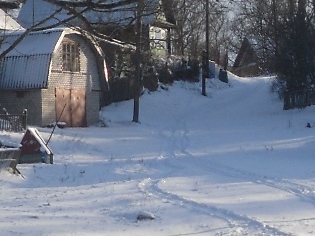 Зимний пейзаж белорусской деревни Гостилы: старый деревянный сарай с красными дверями в снегу, традиционные сельские строения, жизнь в деревне Белоруссии, семейные воспоминания и исторические корни в живописной местности у реки Березина
