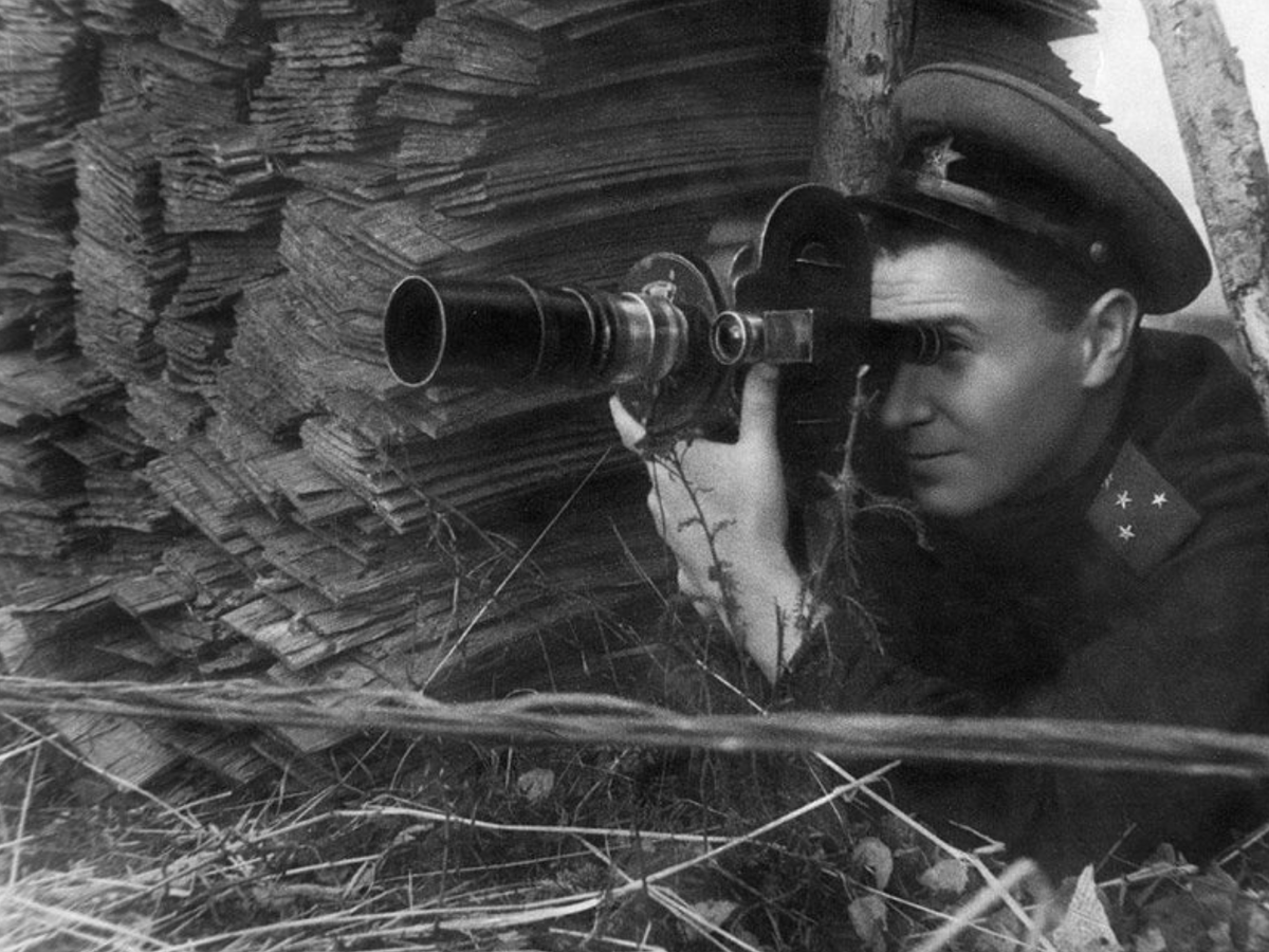 Фронтовой оператор Семен Школьников. 1943-1944. Госкаталог. Федеральное государственное бюджетное учреждение культуры "Государственный центральный музей кино". В укрытии, на траве лежит оператор С. Школьников с ручной кинокамерой, одет в гимнастерку с погонами, фуражку
