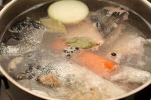 Варим бульон. Кладём в кастрюлю головы, кости и крупные куски рыбы (примерно 700–800 г из общего количества) — заливаем холодной водой так, чтобы покрыть рыбу, и доводим до лёгкого кипения на среднем огне. Снимайте пену шумовкой, иначе бульон будет мутным.