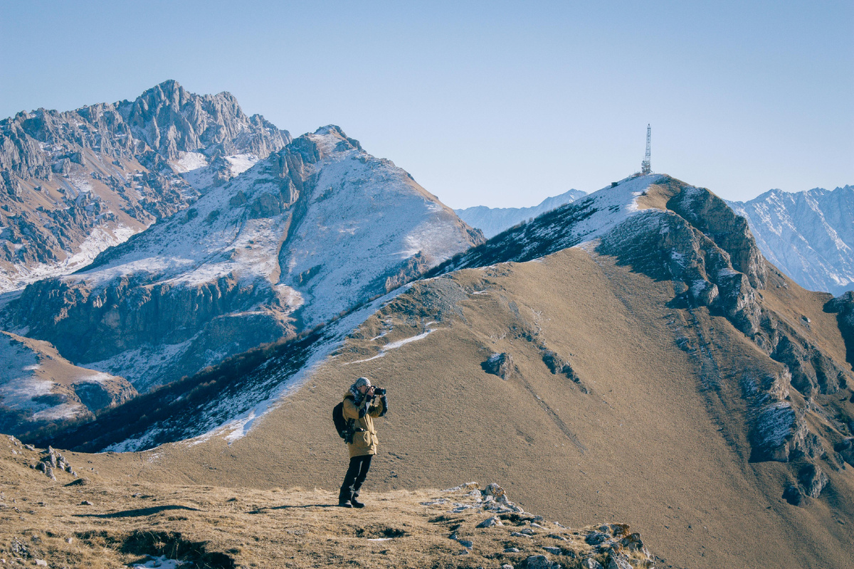 Путешественник идёт по горной тропе среди величественных пиков, наслаждаясь моментом и свободой пути.