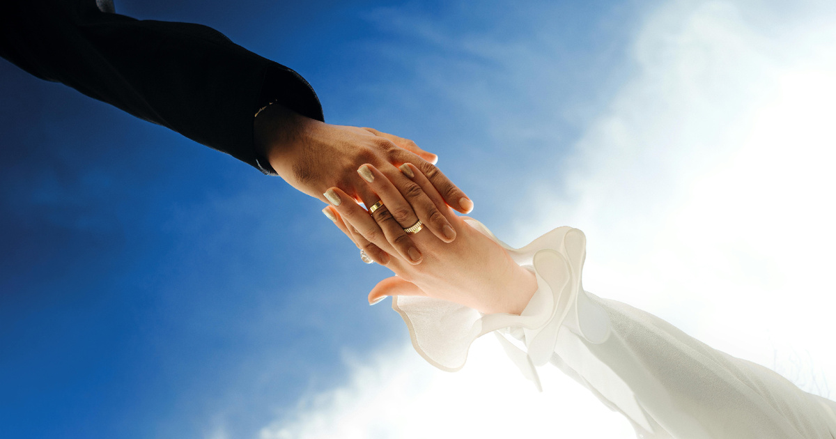 Пара держится за руки на фоне яркого неба, символ поддержки и взаимной опоры