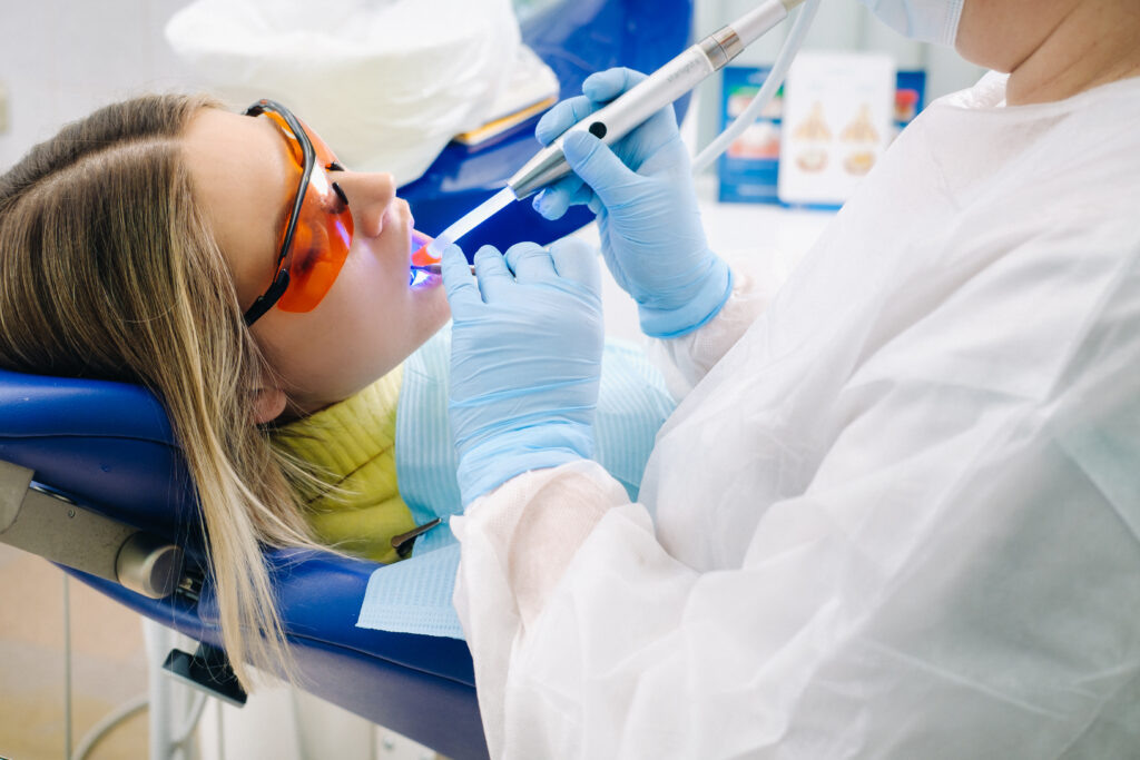    A young beautiful girl in dental glasses treats her teeth at the dentist with ultraviolet light. filling of teeth. Стоматология Во Владимире