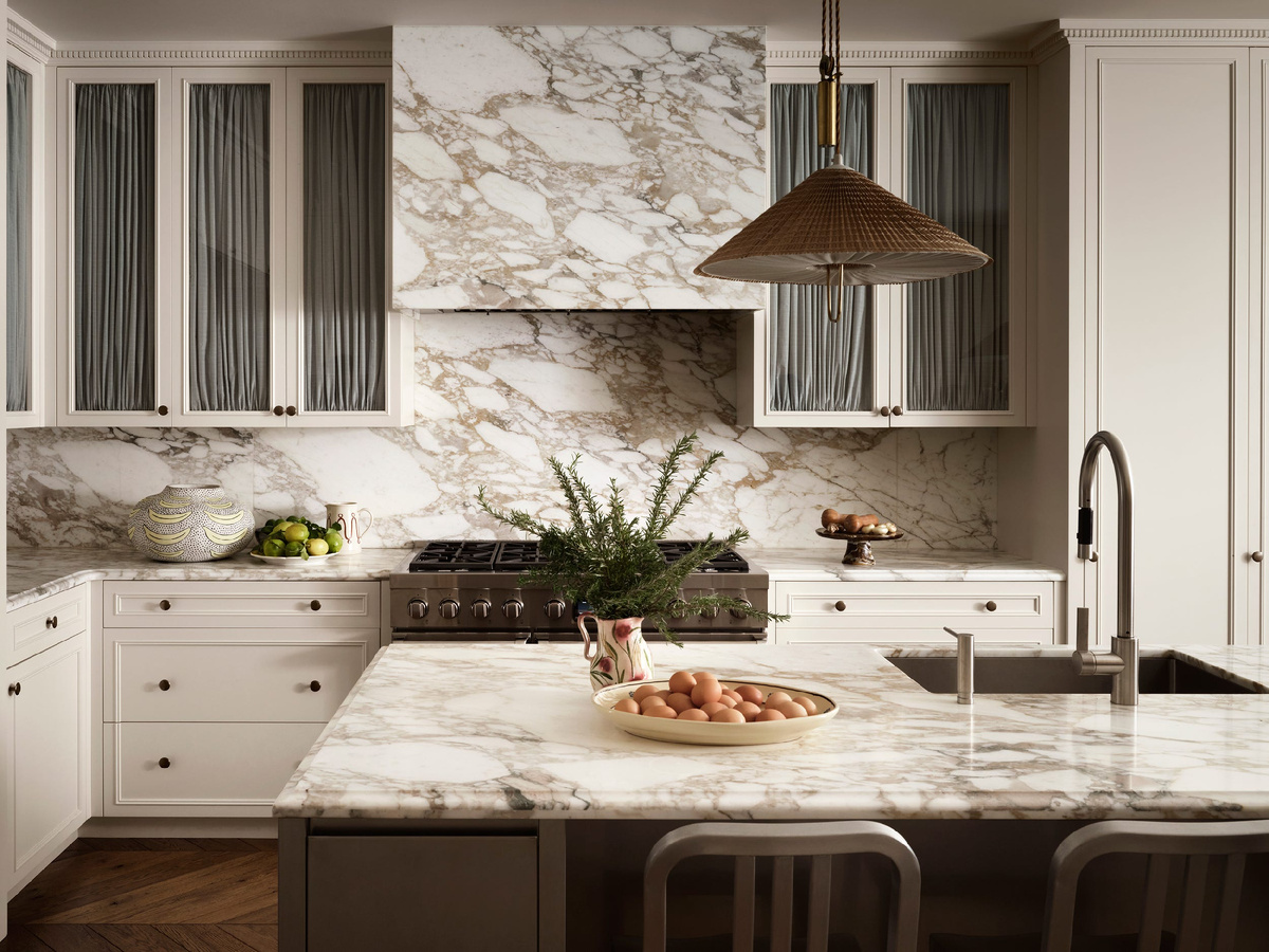Столешница острова из мрамора с динамичным рисунком вен в оттенках кофе с молоком поддержана стеновой панелью из того же материала