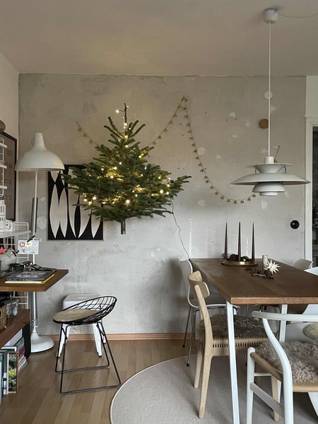 Искусственную елку можно оригинально прикрепить к стене, подсвеченной красивой гирляндой.