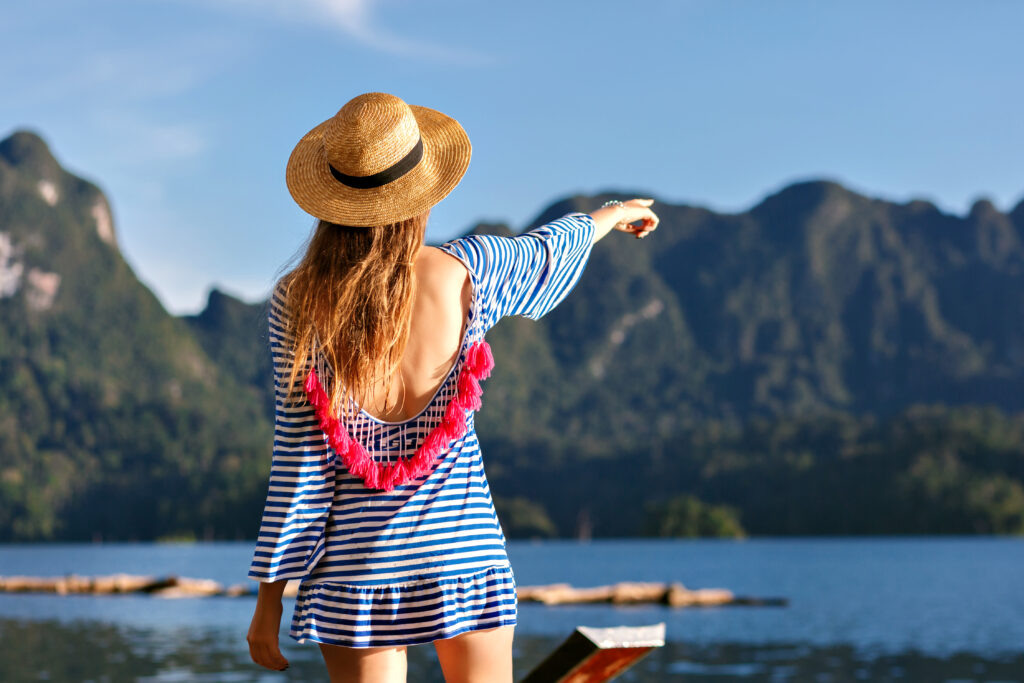    Young pretty blonde woman with long hairs, wearing vintage hat and bright sexy trendy dress looks to the mountains and lake, show her hand, amazing summer adventures. stepnaya