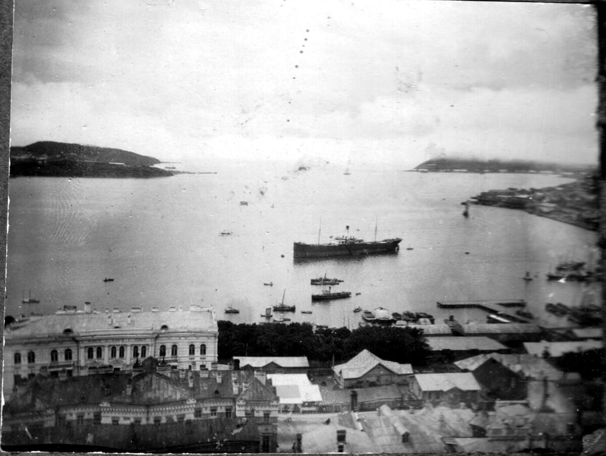 Вид с Алексеевской Сопки на бухту Золотой Рог 1904 – 1905 На переднем плане за крышей почтамта, построенный в 1903 году, дом Я. Л. Семенова (современный адрес Светланская ул., 46).Автор: Струпов Алексей Алексеевич, московский врач, мобилизованный на Русско-Японскую войну/Чёрно-белое Приморье