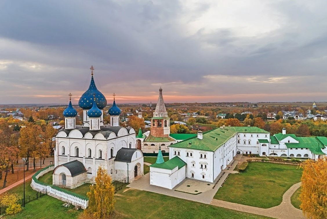 Суздальский Кремль осенью, вид сверху: храм с синими куполами, белокаменные здания и яркие осенние деревья