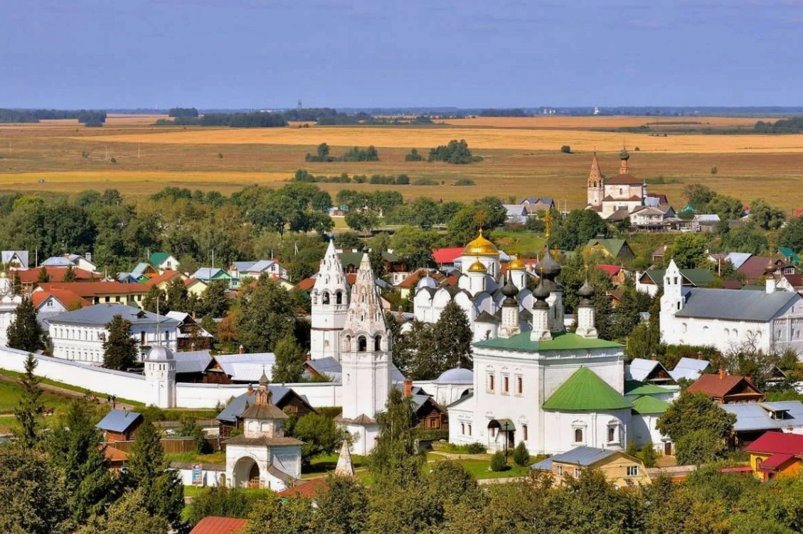 Панорама Суздаля летом: белокаменные монастыри, купола церквей и деревянные дома на фоне полей и зелёных холмов