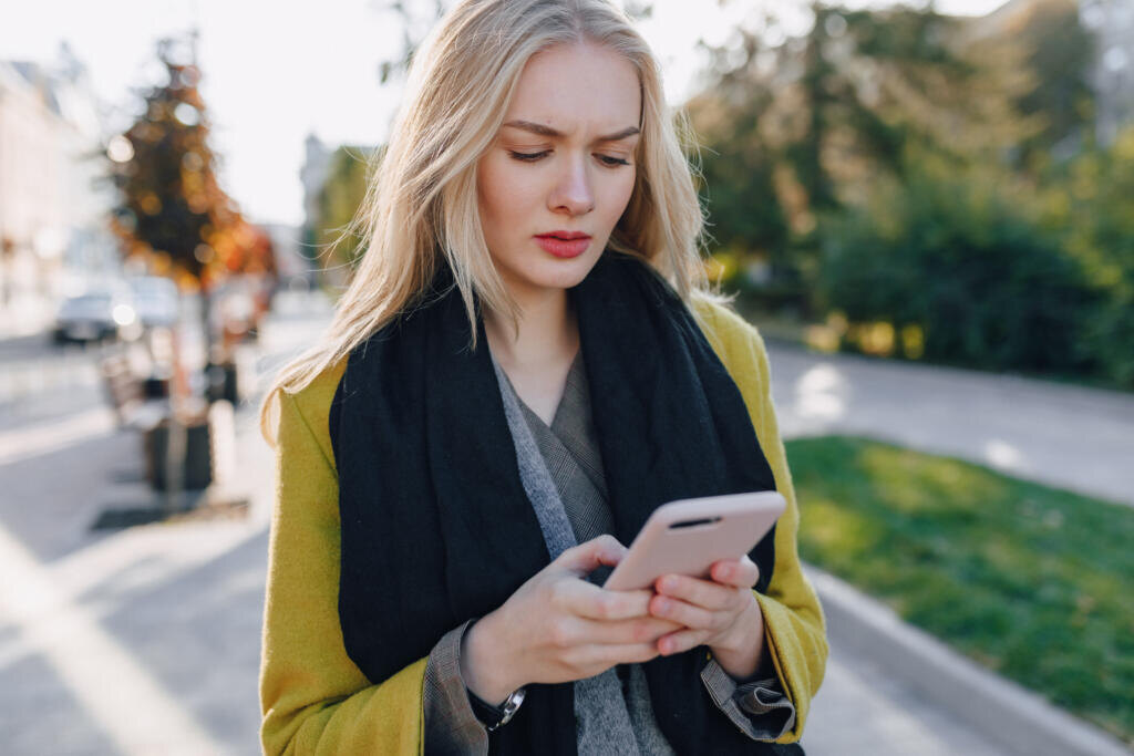   cute emotional attractive blonde woman in coat with smartphone walks the city street. communication during the walk, lifestyle, street in good weather. Журналист