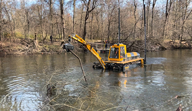    Экскаватор-амфибия, способный передвигаться и по воде, и по суше, вытаскивает из реки упавшие деревья и крупный мусор