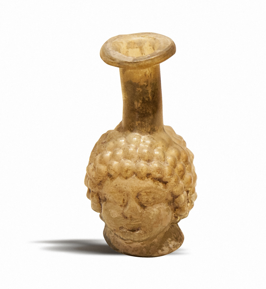 Древнеримский флакончик в форме головы ребенка или юноши (I–III вв. н. э.), выдутый в форму. И да, римляне действительно массово производили такую «головную» посуду. Возможно, потому что это выглядело мило… а возможно – потому что им просто нравилось смотреть на такие штуки, стоящие на туалетном столике.