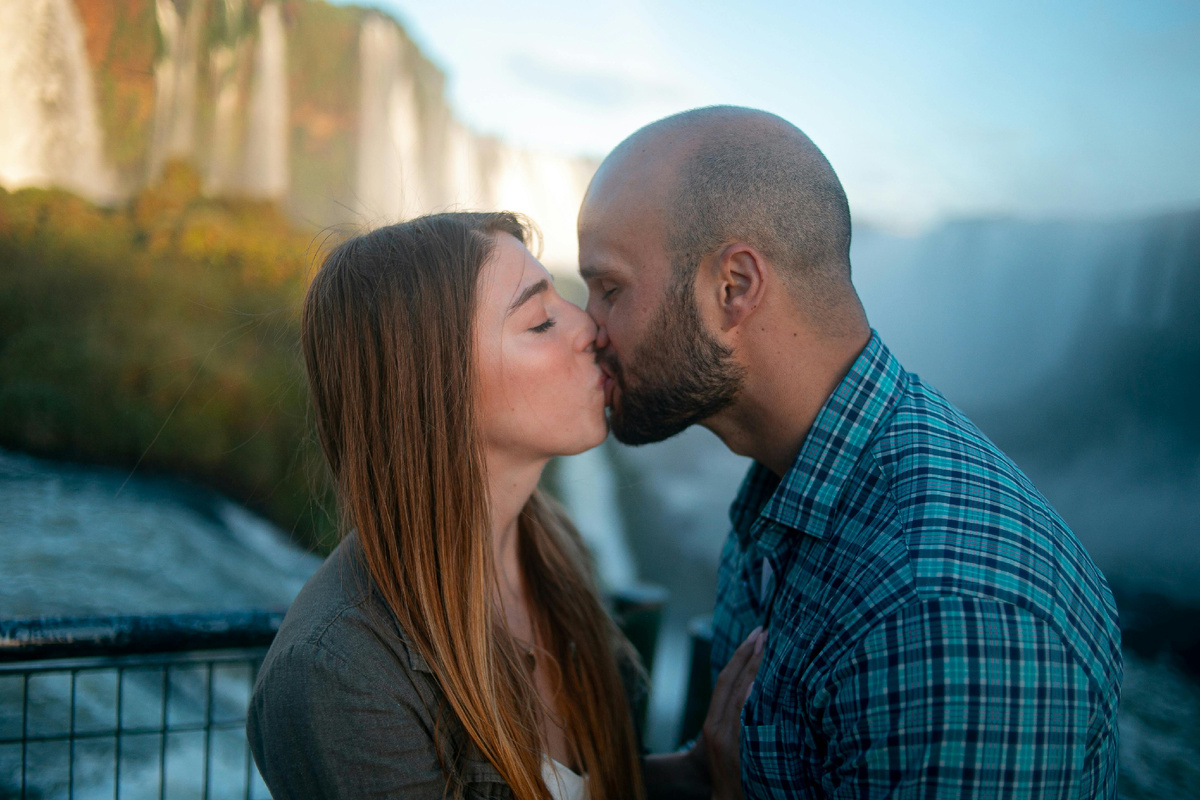 Пара целуется на набережной на фоне водопада — тёплый момент, к которому приводит лёгкая и искренняя переписка. Как начать диалог в переписке.