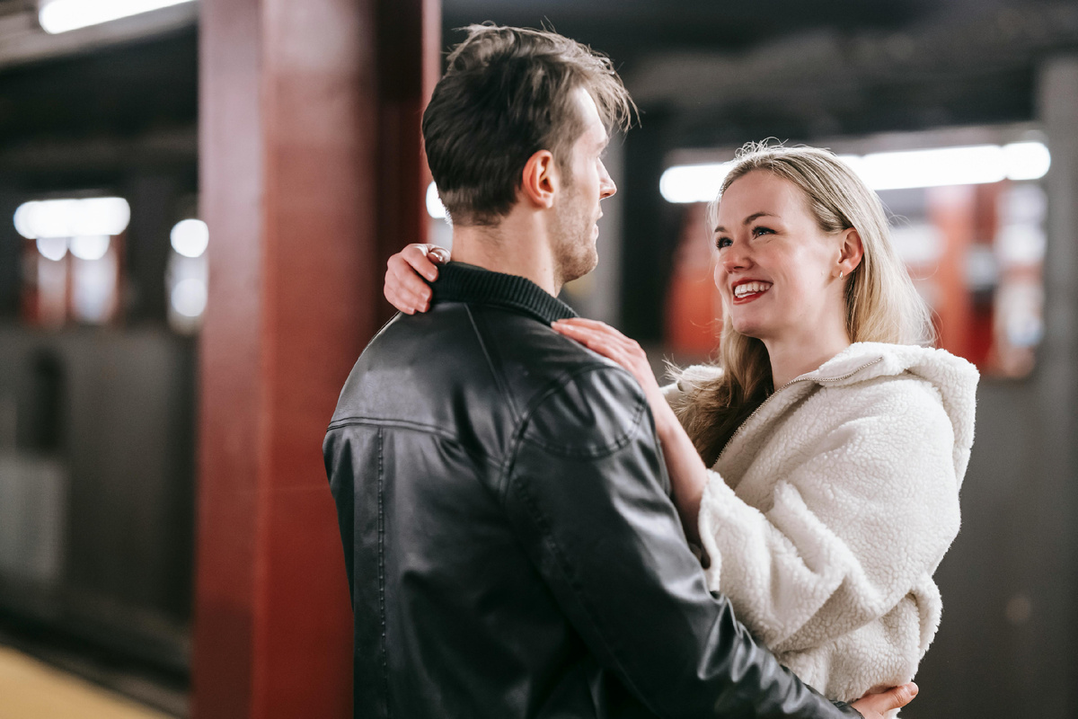 Пара обнимается и улыбается друг другу на платформе метро, создавая атмосферу радости и взаимного притяжения.
