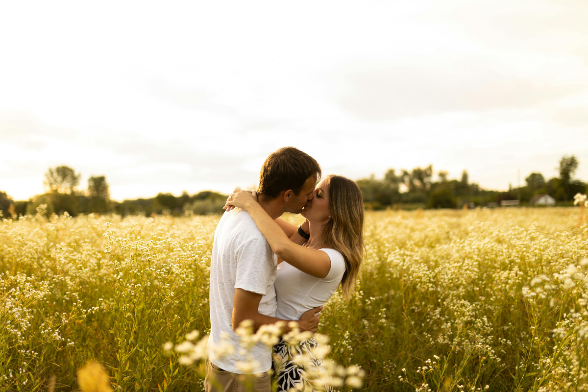 Пара целуется в поле на закате, обнимая друг друга среди тёплого золотистого света.