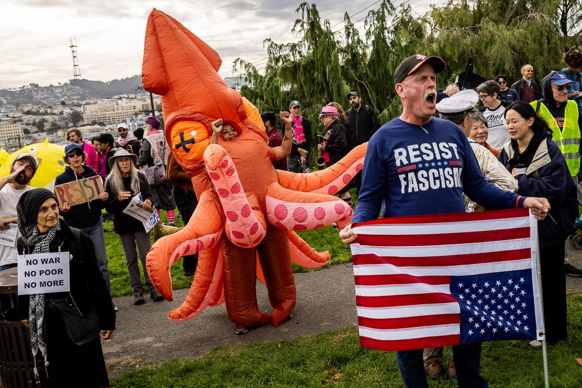   Кристина Ливингстон (в центре), одетая в надувной костюм кальмара, слушает выступающего активиста на площади Алта-Плаза во время акции «Люди важнее миллиардеров» в Сан-Франциско, США 
Stephen Lam / San Francisco Chronicle via Getty Images