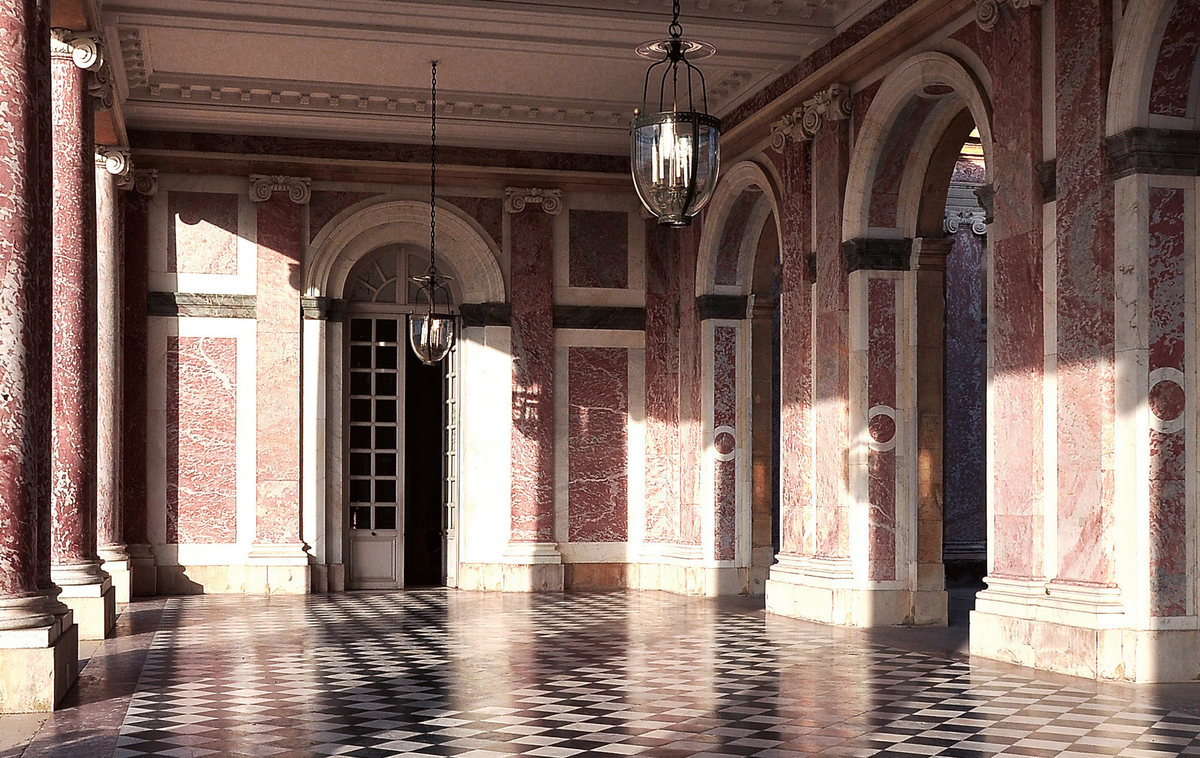 Розовый мрамор Гранд-Трианон
Людовик XIV питал особую любовь к мрамору, что нашло отражение в обильном его использовании в Версале. При реконструкции Большого Трианона в 1687 году архитектор Франсуа Мансар выбрал для колонн и пилястр розовый мрамор. Этот ценный материал доставлялся из карьеров в Кунес-Минервуа, у подножия Пиренеев. Далее его путь лежал по реке в Бордо, затем по морю в Гавр, и, наконец, по Сене он прибыл на стройплощадку, где сам король лично контролировал ход работ.
Поместье и территория Гранд Трианон, Перистиль, Версаль.