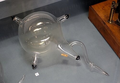 Трубка Вильяма Крукса. Обратите внимание на желтоватый оттенок стекла трубки. Это всё из-за оксида свинца, добавленного в стекло, для того чтобы защитить трубку от воздействия температуры. Чтобы она не расплавилась во время экспериментов. Однако именно оксид свинца, не пропускающий рентгеновское излучение, мешал его открытию. 