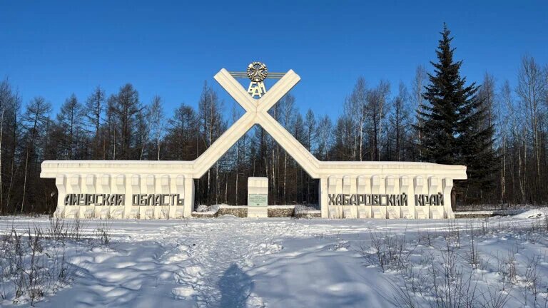 Живописный вид на Амурскую область: спокойная речная бухта, покрытые лесом холмы и яркая летняя зелень под чистым голубым небом.