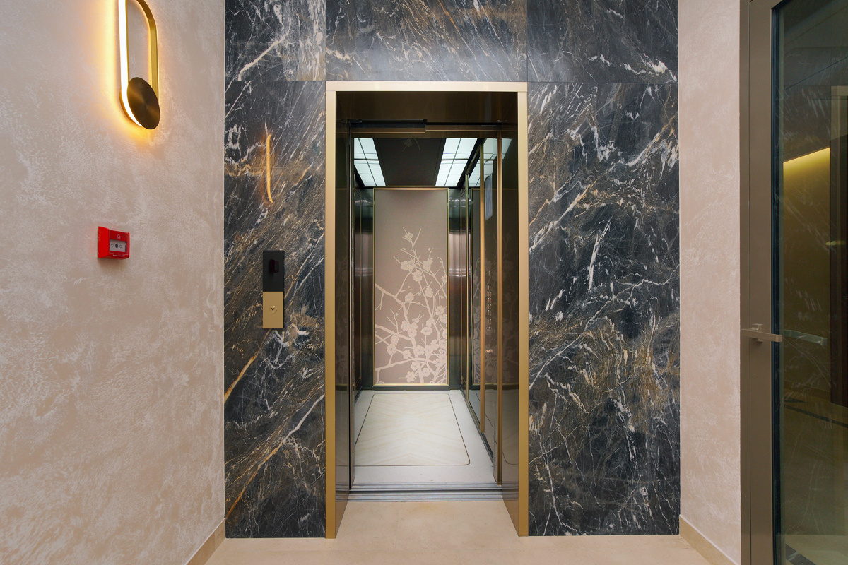 Внутри лифта – настоящее произведение искусства: кожаное панно на задней стенке в изящной раме цвета шампанского, стены с теплой текстурой дерева. 