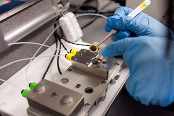 Фото 1.  Исследователи прикладывают небольшой чип круглой формы на прибор для измерения адсорбции PFAS молекулярным покрытием.  Фото John Zich