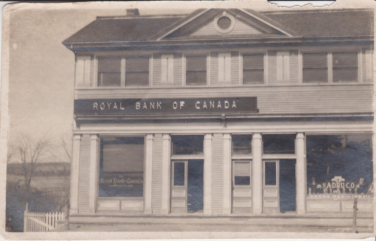 То самое здание отделения Royal Bank of Canada в Шубенакади, каким оно было в 1930‑е: деревянные колонны, витрины, соседняя витрина аптеки — провинциальная идиллия до перестрелки.