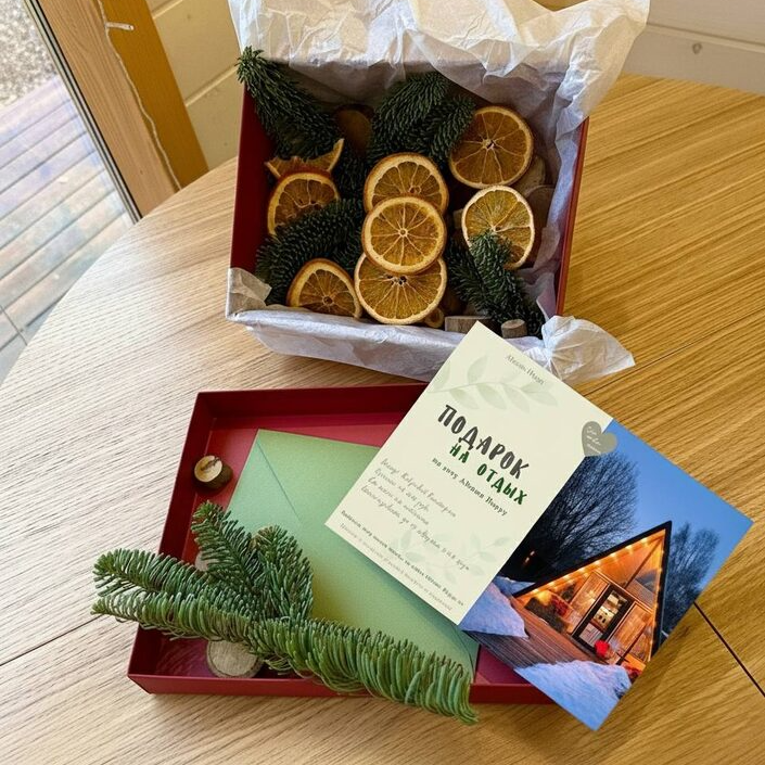 Красивый подарочный конверт с сертификатом на фоне уютного A-frame домика зимой - идеальный подарок на день рождения