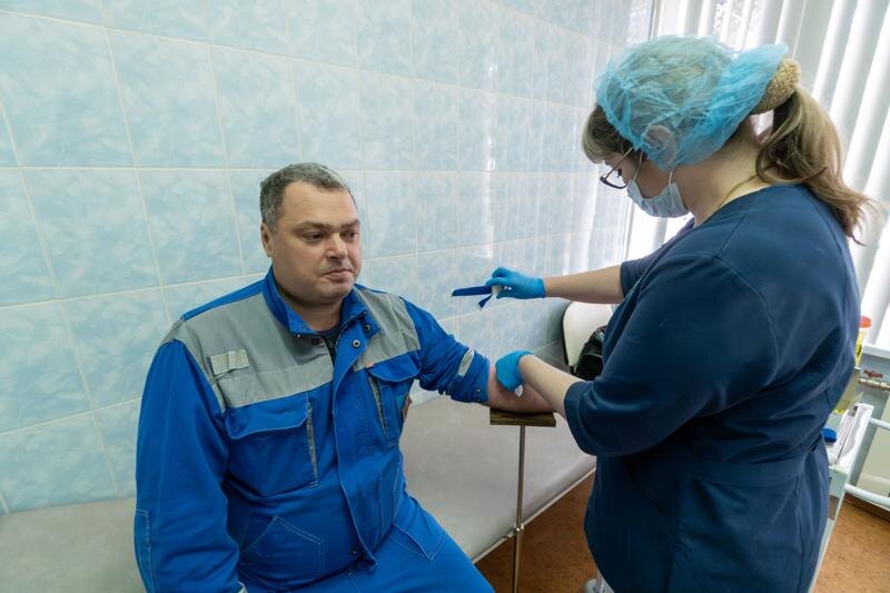    Врач берет кровь у сотрудника завода