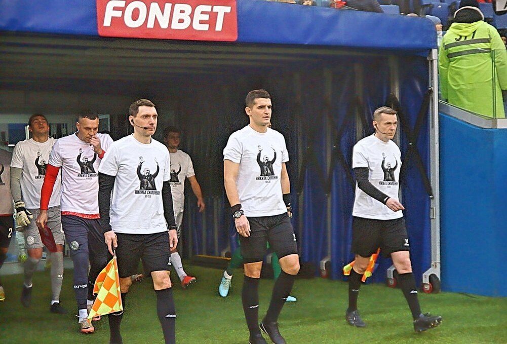 Бригада судей и стартовые составы команд выходят на поле в майках, посвященных первому вице-президенту РФС Никите Симоняну, который скончался 23.11.2025.