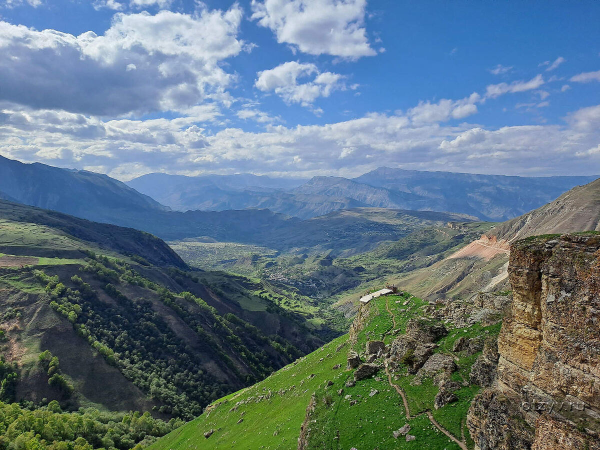 Горная панорама Дагестана с зелёными склонами и широкими долинами под облачным небом.