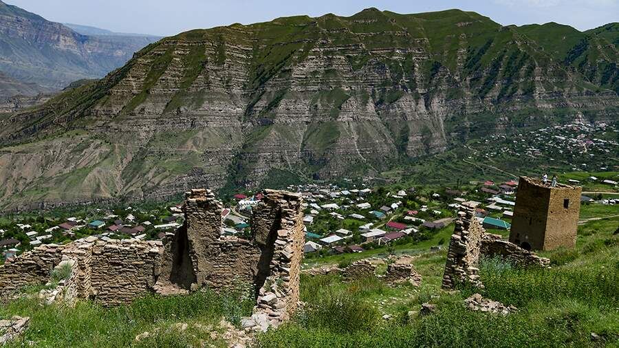 Развалины старых построек в горном селе Дагестана с панорамой на долину и массивный хребет на фоне.