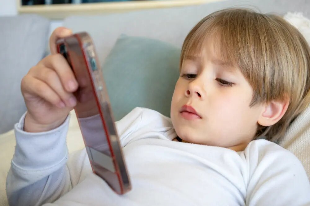 Ребёнок смотрит в телефон с близкого расстояния, находясь в неудобной позе