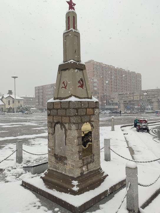 Памятник в Аньда на фоне привокзальных кварталов городка. 