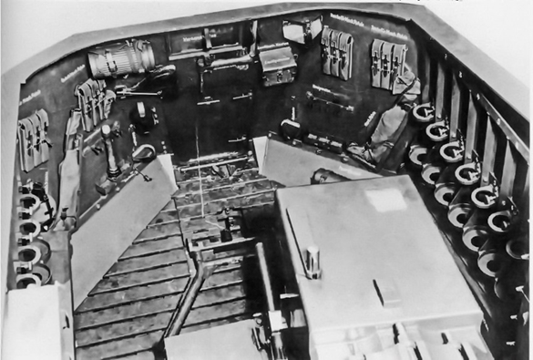 вид на заднюю часть орудийной рубки. На переднем плане – массивный казённик 128-мм орудия 12,8 cm K 40 L/61, на скосах заднего борта закреплены 4 подсумка для магазинов к пистолет – пулемётам MP-38(40), гофра с противогазом, на решетчатом деревянном полу лежит в положении «по-боевому» фиксатор казённой части орудия, которым люлька арт. системы крепилась (фиксировалась) на марше. Хорошо виден задний прямоугольный люк – дверь, который использовался экипажем для входа – выхода в САУ, а также погрузки БЗ. По причине большого размера казённой части орудия и размещения БЗ вдоль бортов, боевое отделение (хоть и не маленького размера!) просторным не является!