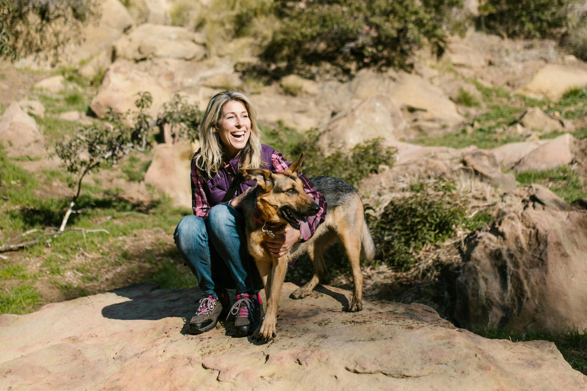 Женщина отдыхает на камнях во время прогулки по природе и обнимает собаку — тёплый момент в путешествии на свежем воздухе.
