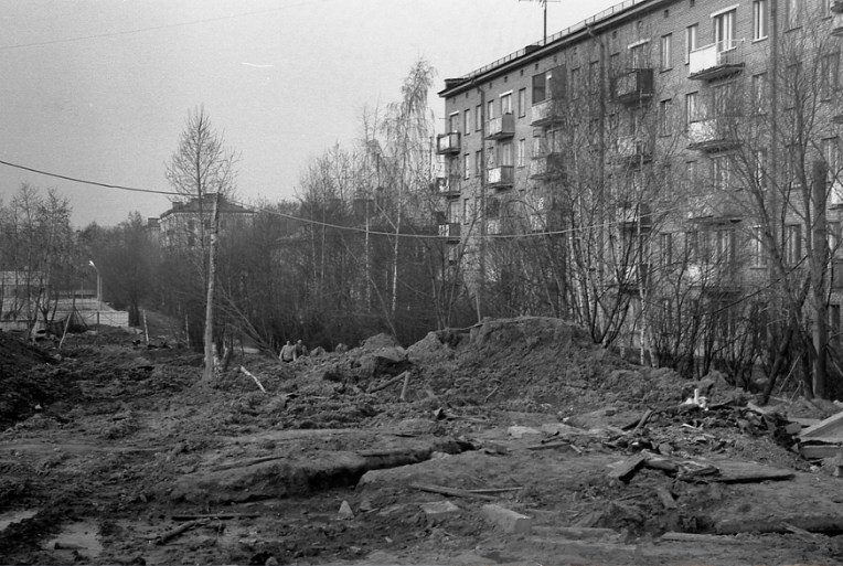Вид на Талдомскую улицу в сторону от Весенней улицы. На переднем плане подготовлено место под строительство детского сада. Вместо пятиэтажки справа стоит современный жилой дом. За ним за деревьями трёхэтажный жилой дом и следом здание школы. Все их уже снесли. 