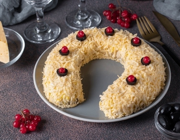    Festive puff salad in shape of horseshoe with chicken, eggs, cheese and olives on brown table, Close-up Glavred