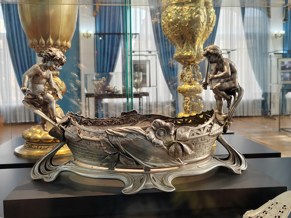 Подставка для вазы. Германия. Фирма "Лазарус Позен".  Около 1890-х гг. Серебро: штамповка, гравировка, литьё, чеканка. Подставка для вазы является характерным образцом стиля модерн, получившего самобытное прочтение в Германии в 1890-1910 -е гг. На вазе есть гравированная надпись: "МГК ФК И СПОРТА. ЮНОШЕСКОЕ ПЕРВЕНСТВО МОСКВЫ ПО ГИМНАСТИКЕ. ПЕРЕХОДЯЩИЙ ПРИЗ" и "1951 г. - ЦЮСШ-МПС". Надпись является  свидетельством истории бытования предмета, ставшего призом на спортивных соревнованиях в советское время. /Астраханский музей-заповедник. Выставка «От Возрождения до модерна». 2025 г.