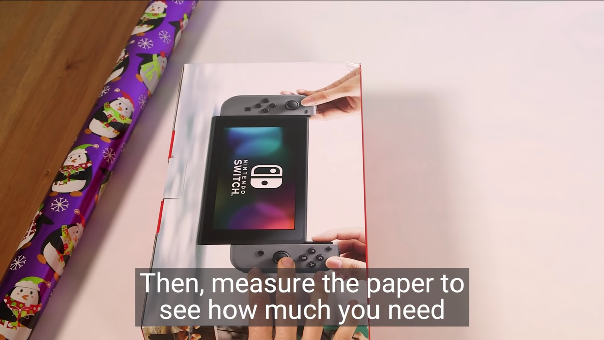    Шаг 1. Раскладываем бумагу на стол. Сверху кладем подарок в коробке. Располагаем коробку так, чтобы сверху и снизу осталось достаточное количество бумаги для загиба на боках. Отрезаем ненужное.YouTube / Business Insider