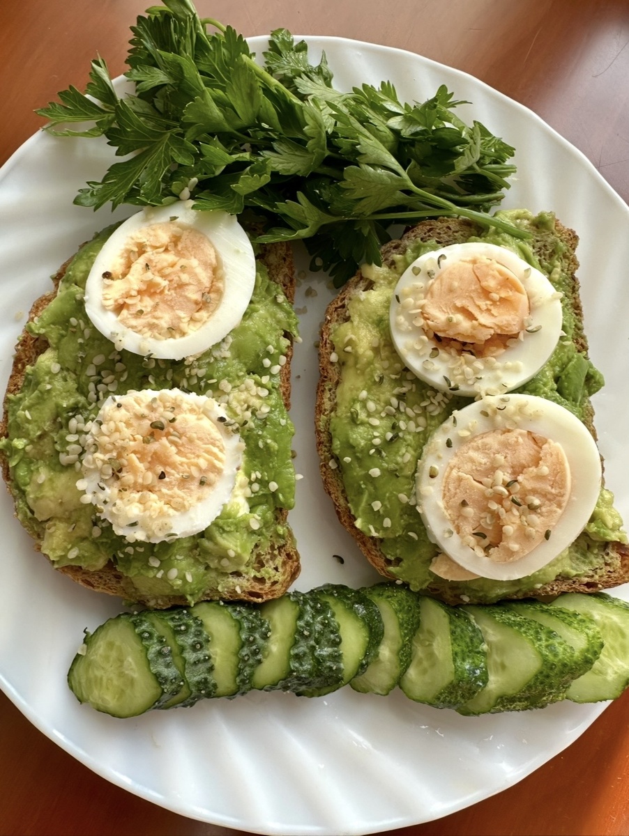 Цельнозерновой тост с пюре из авокадо вареным яйцом и семенами конопли, свежие огурцы и пучок петрушки.
