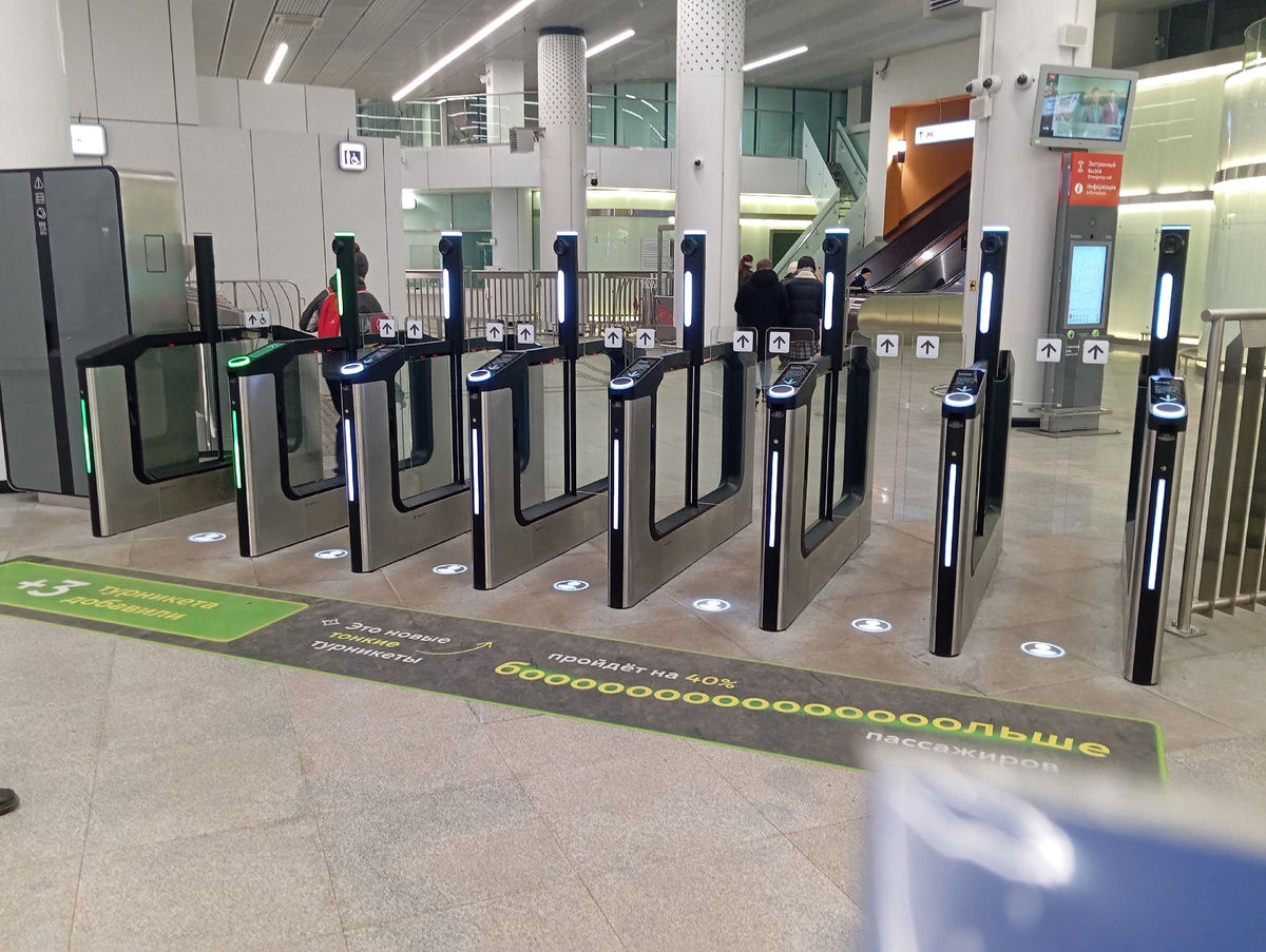 Линия новых турникетов в вестибюле: тонкие стойки, световые полосы, разметка на полу про ускорение прохода.