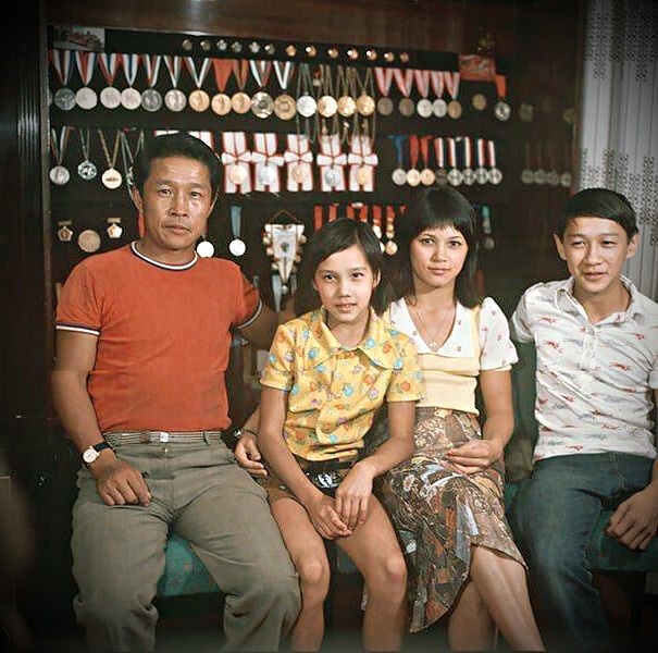 Гимнастка Нелли Владимировна Ким с отцом, братом и сестрой на фоне своих спортивных наград.