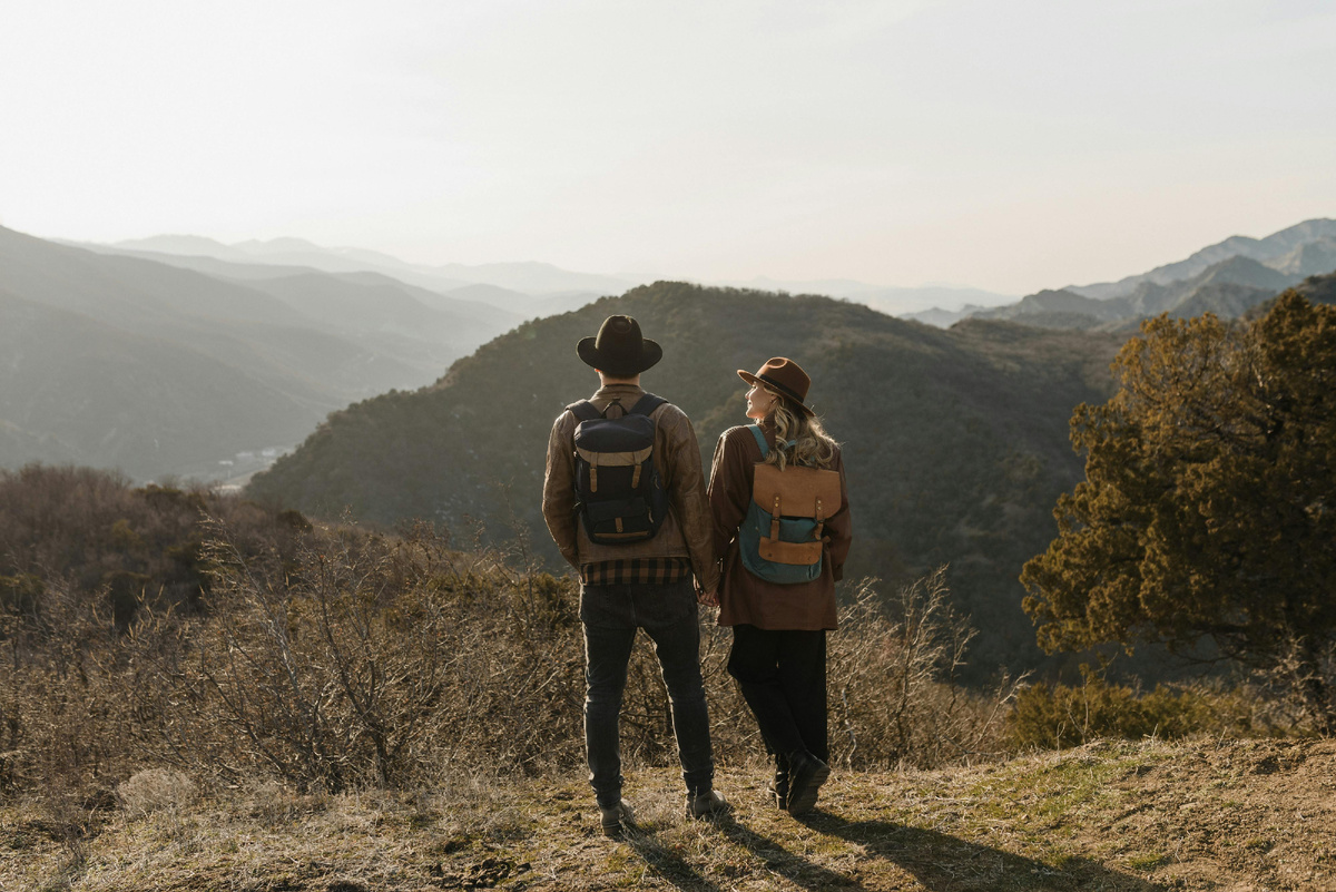 Путешественники с рюкзаками стоят на вершине холма и смотрят на горы — первое знакомство с новым маршрутом и ощущение свободы в путешествии