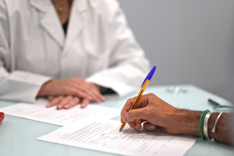 Close-up of doctor and patient filling out medical forms in a clinical office, focusing on hands and documents.