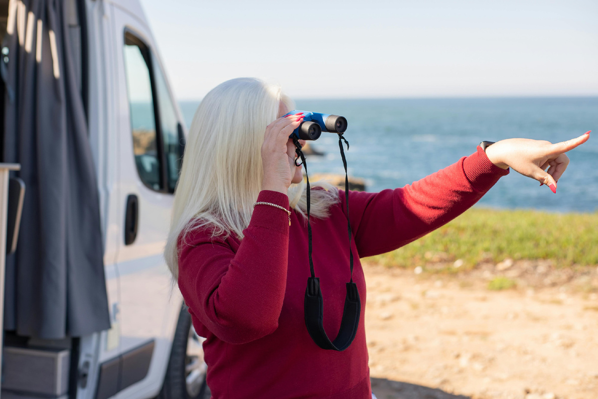 Путешественница с биноклем у берега Байкала, осматривает окрестности и планирует маршрут путешествия
